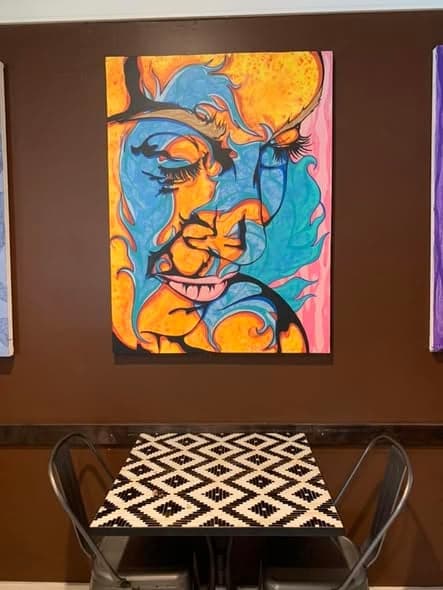 One of the portraits hanging on a dark wall above a patterned cafe table.